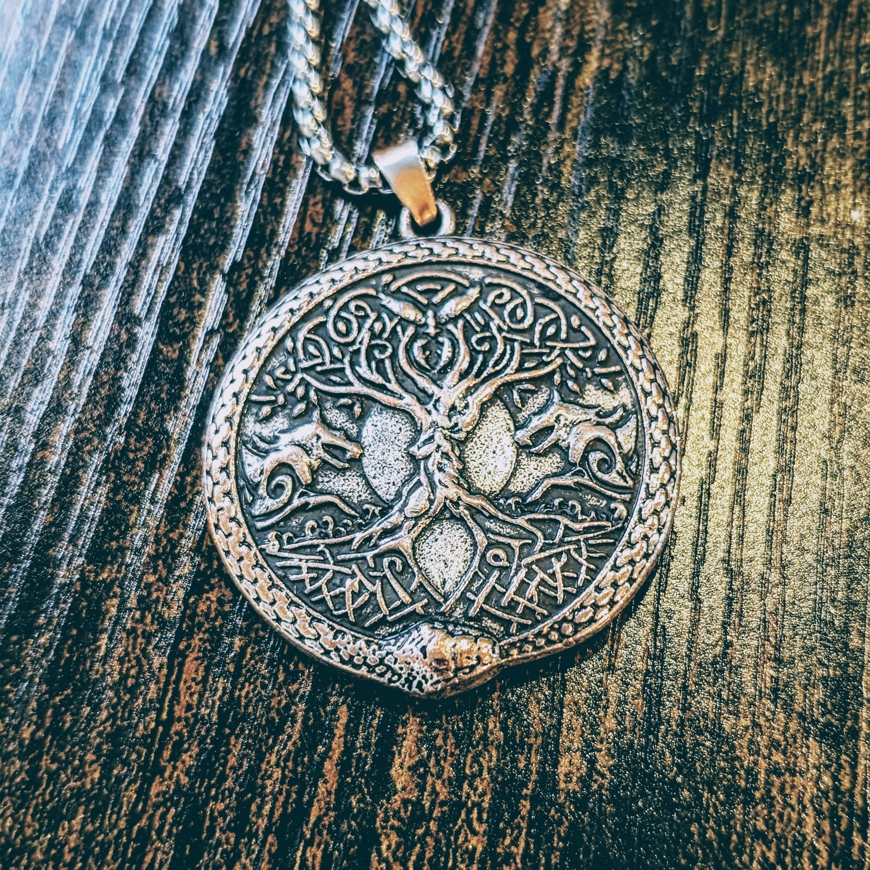 A pendant illustrating Yggdrasil (the World Tree in Norse mythology), one of Odin's wolves on either side, a raven within the bough of the tree while Jormungandr the World Serpent frames the whole pendant.